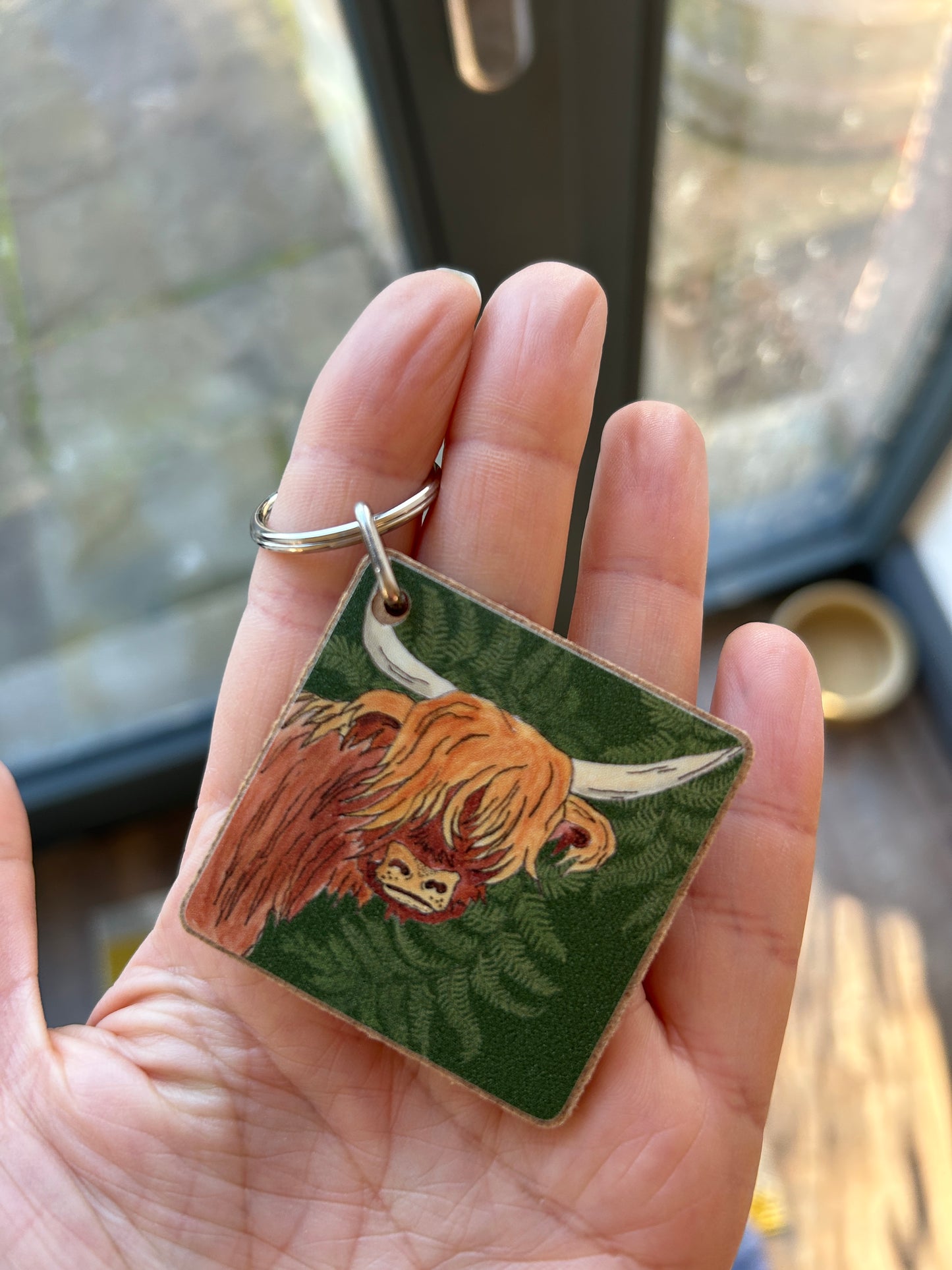 Highland cow illustration on a keyring held in someones hand