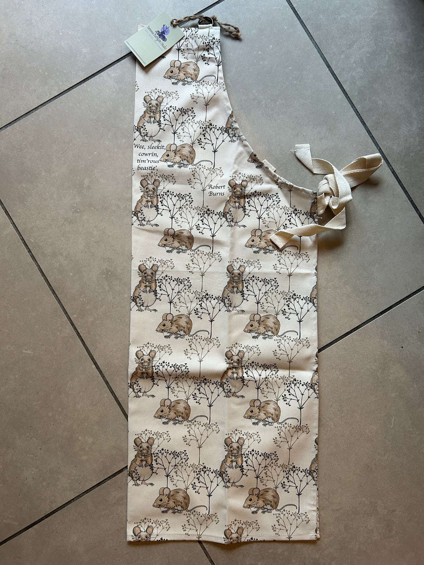 Cotton white apron with mouse and twig design. laid on floor showing binding ties and d loop neck