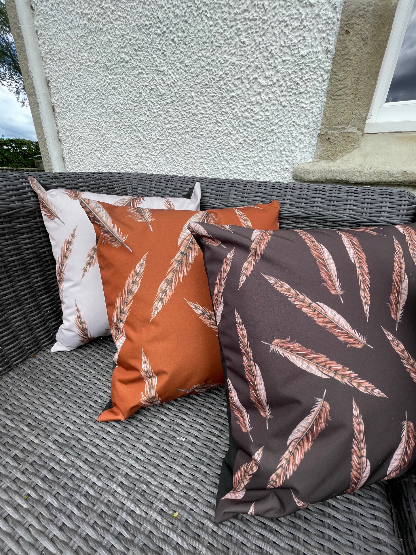 Outdoor water repellent cushions in a pheasant feather illustrated design. in cream, rust or brown. Pictured on outdoor wicker furniture