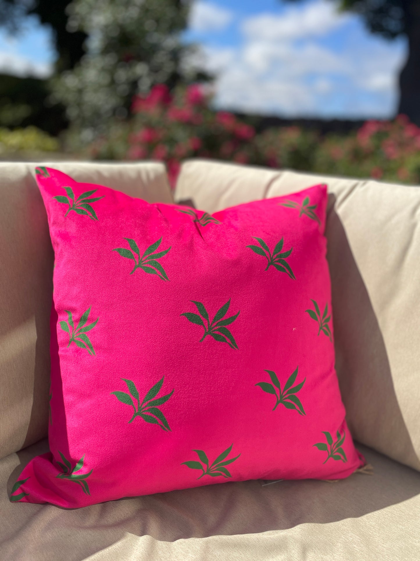 A bright pink, luxurious, velvet cushion with green leaves