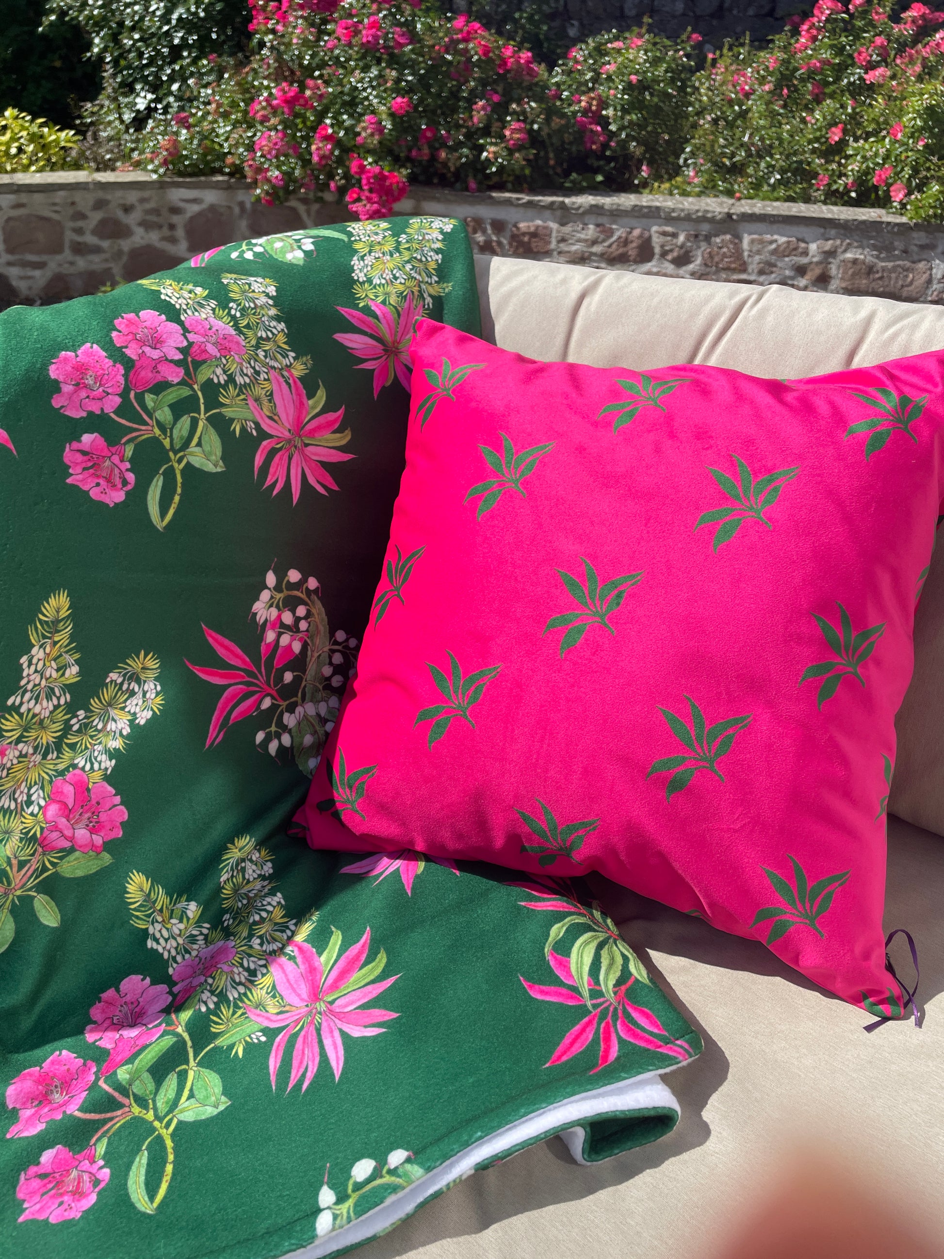 Bright pink, luxury velvet cushion with simple green leaf design, co-ordinated with fleece throw