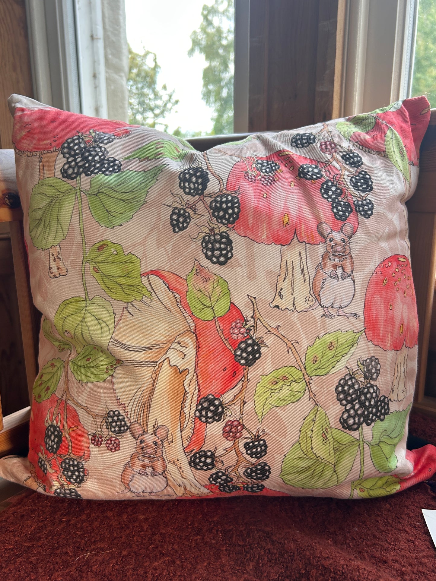 A square cushion with a illustration print featuring blackberries, mushrooms, leaves, and small mice on a light beige background