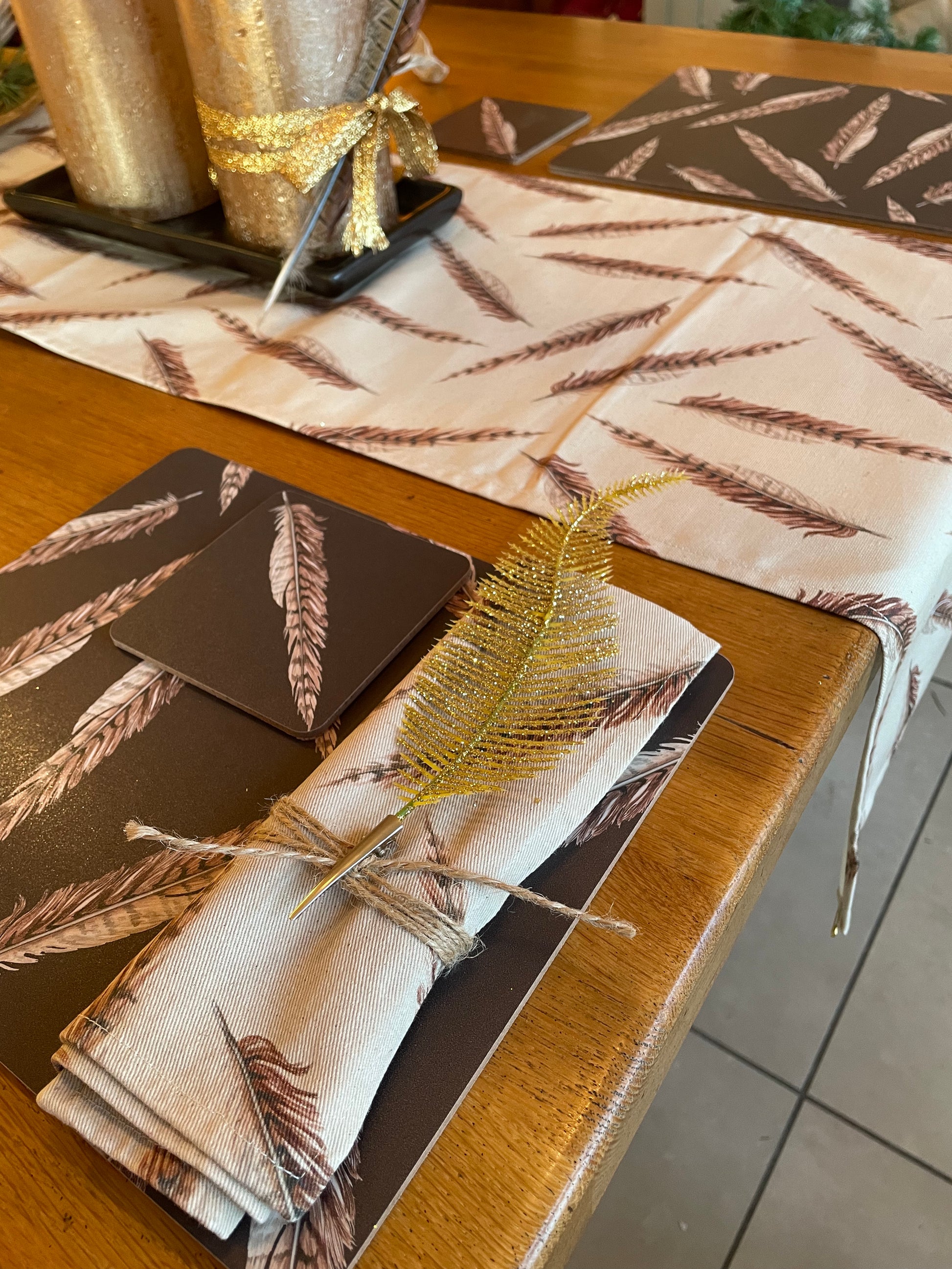 Table setting in pheasant feather design. brown placemats with cream feather napkins tied with gold accessory and matching table runner