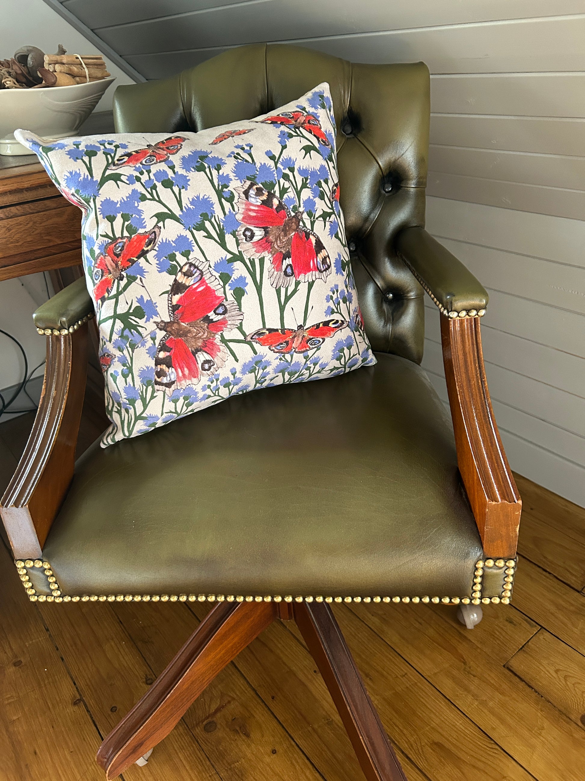 Vanessa Bathgate Butterflies and Thistles cushion design on a green classic leather chair.