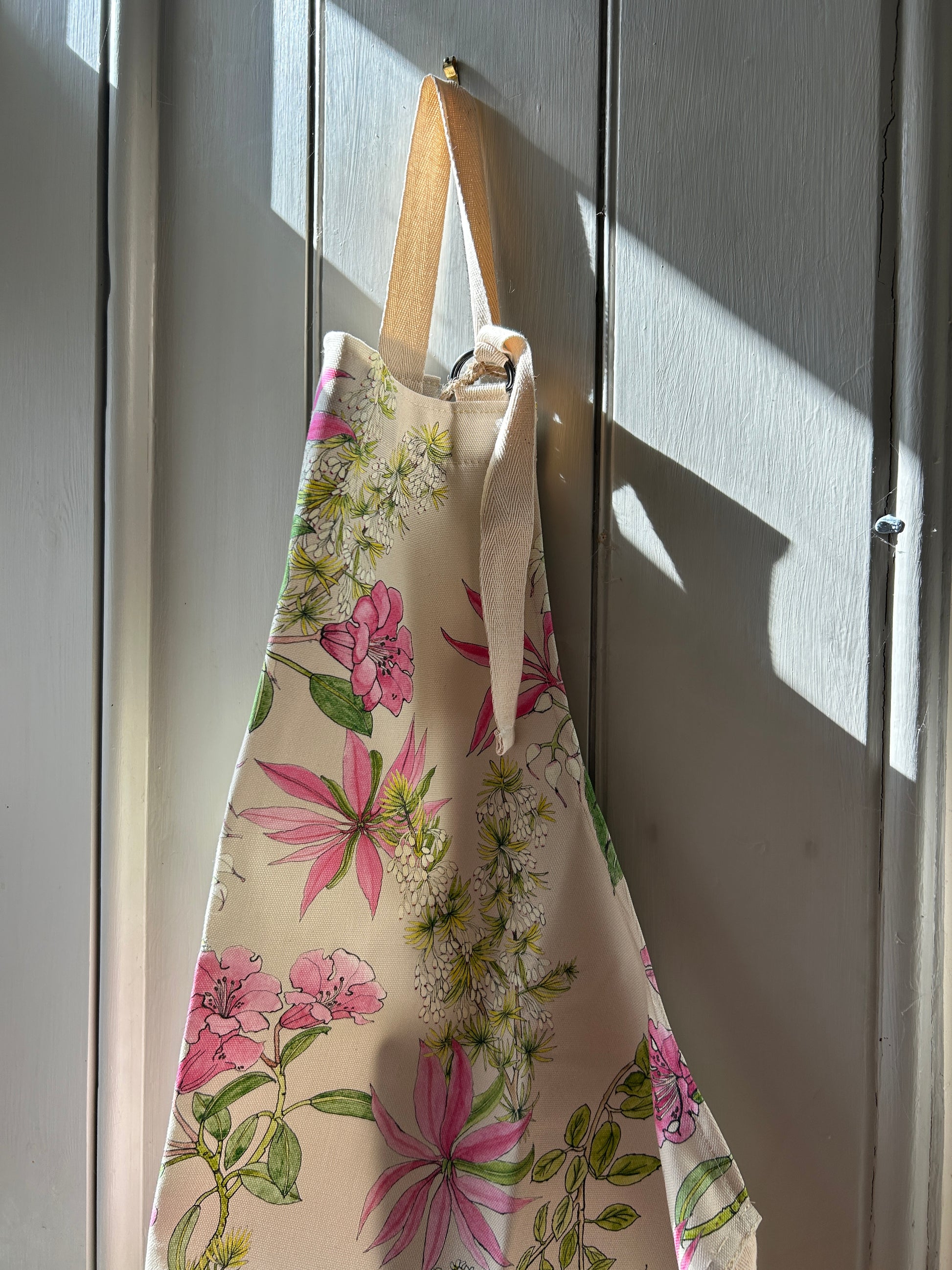 Pink floral designed apron hanging on grey panelling.