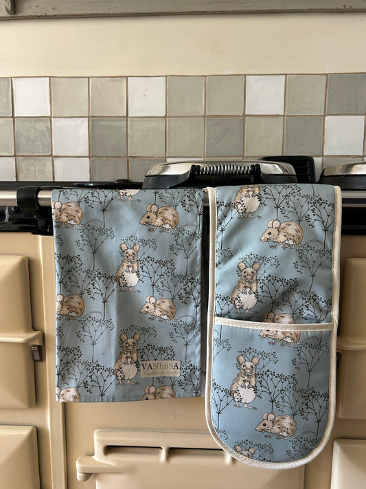 Pair of oven mitts with mouse pattern in soft Blue hanging on a stove.