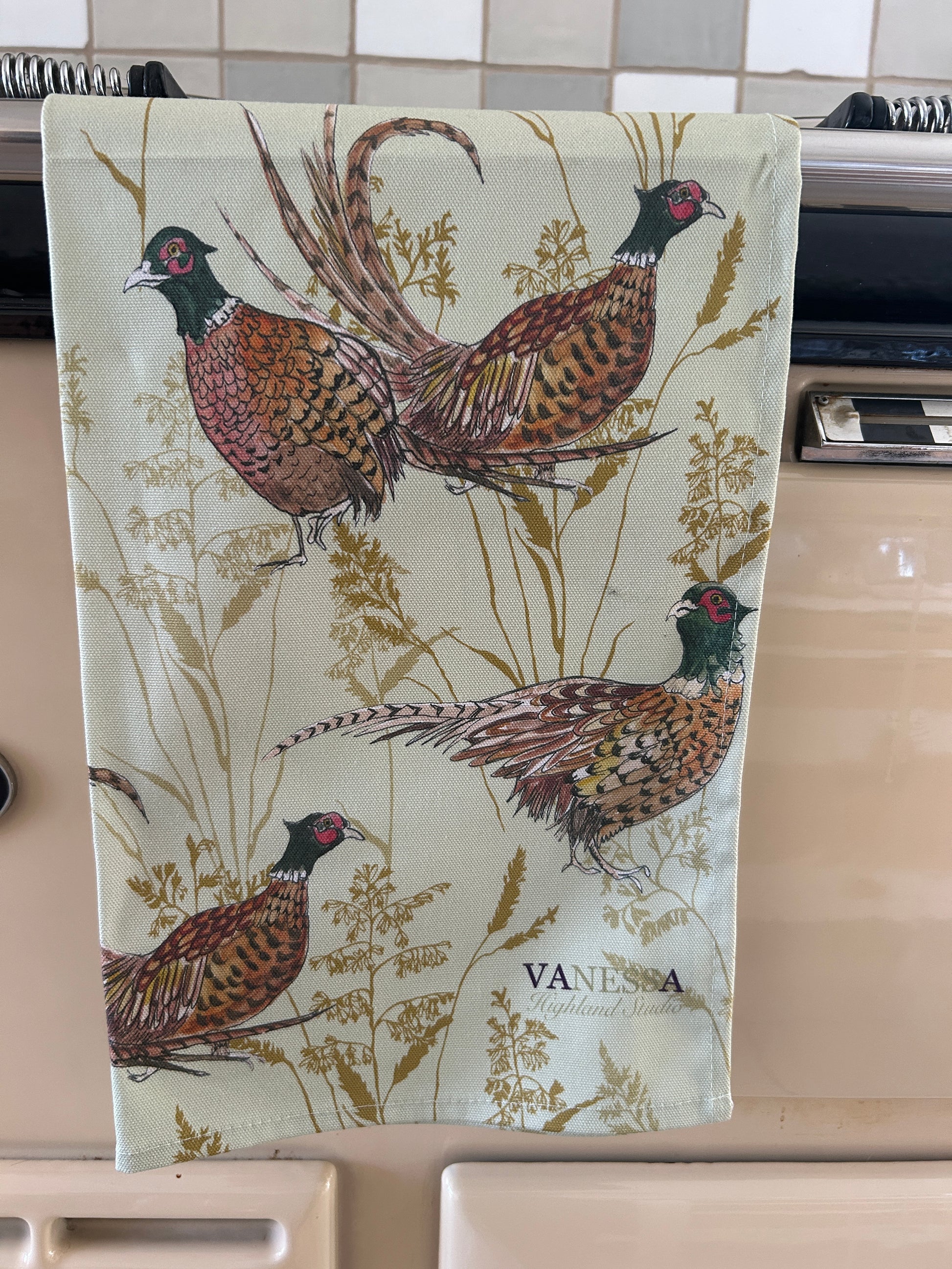 Pheasants and grass illustrated tea towel on a range cooker rail