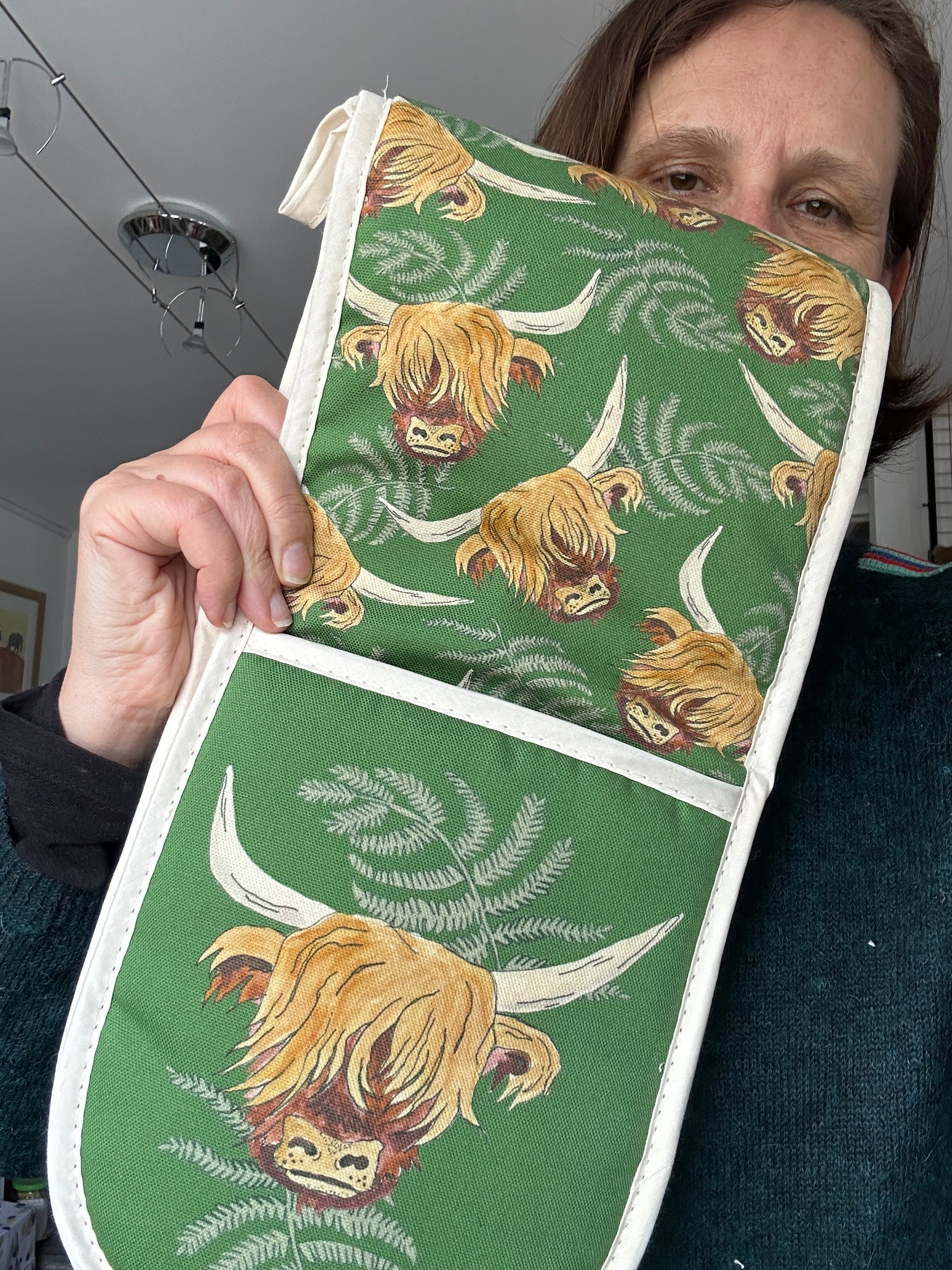 person holding a green oven glove with a Highland Cow design. Coo