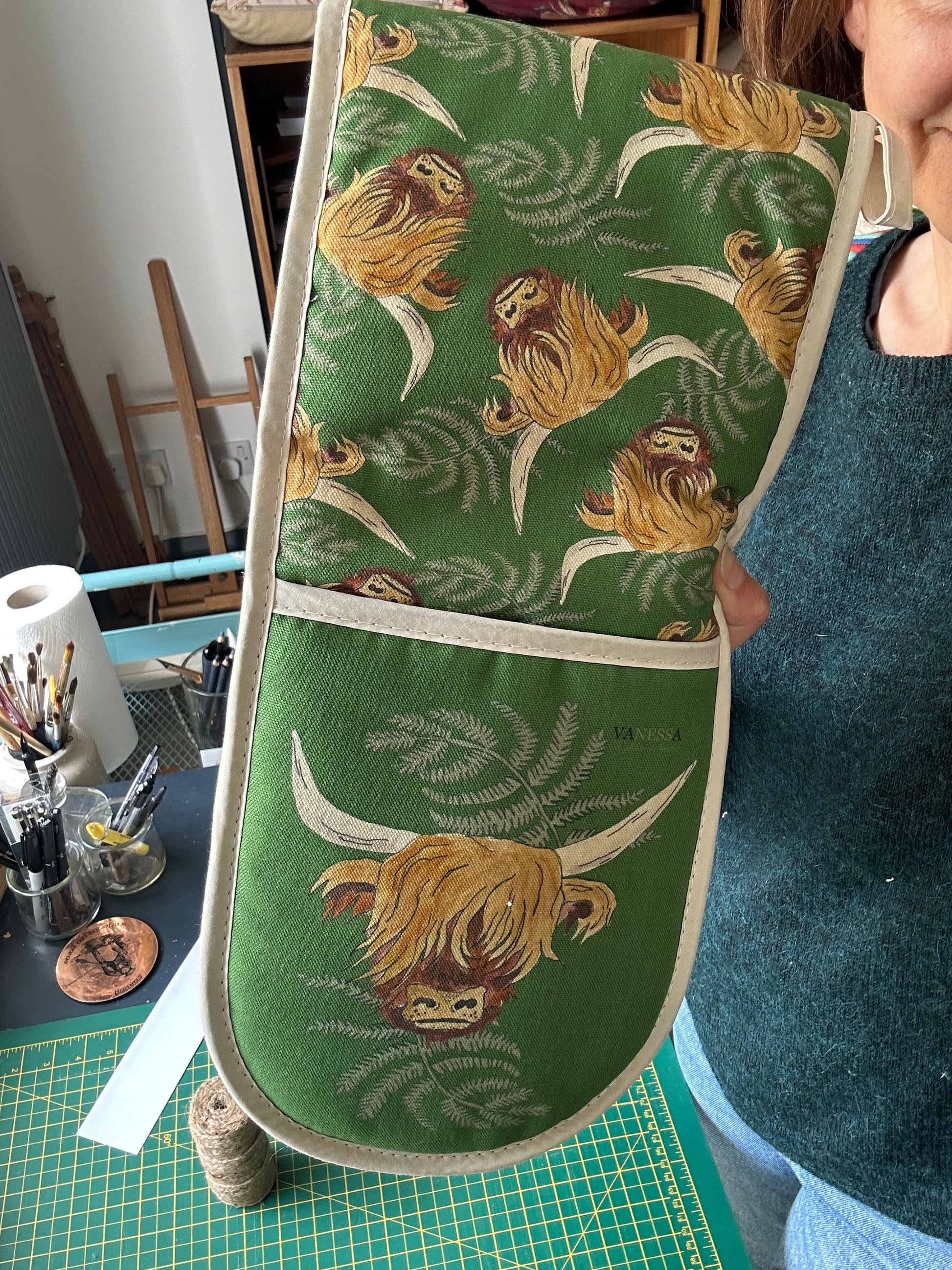 Highland cow on green background with ferns, printed on an oven glove.