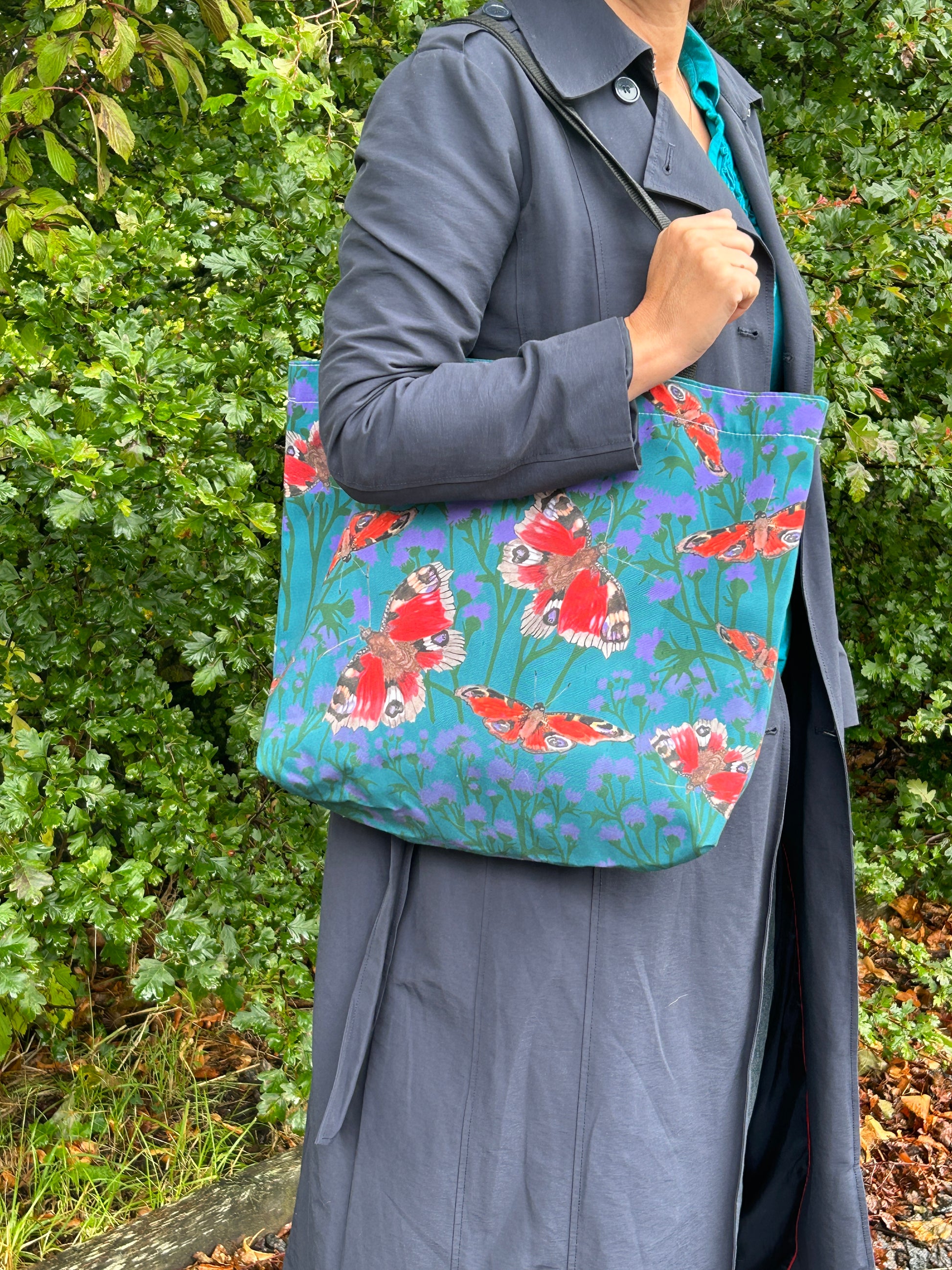 person standing with large shopper tote. Red butterflies and thistle design with teal green background