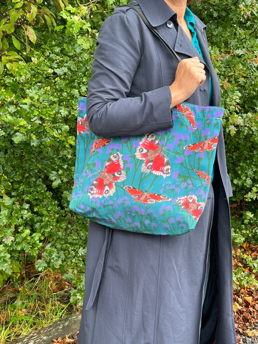 person standing with large shopper tote. Red butterflies and thistle design with teal green background