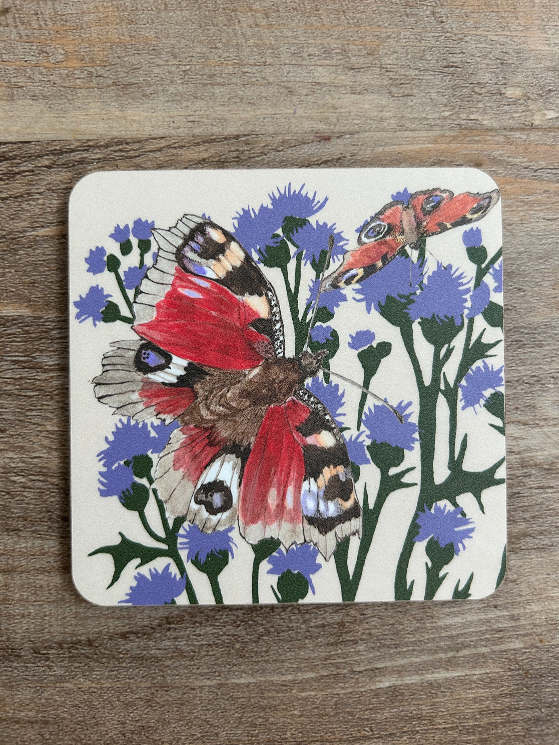 Red and purple butterfly illustration with purple thistle illustration, printed on a cream background coaster