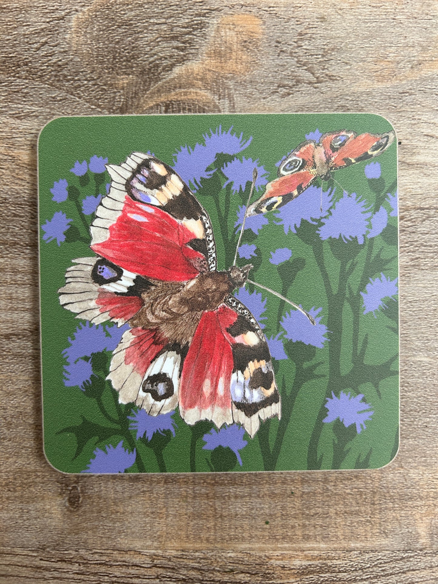 Red and purple spot butterfly on a background of purple thistles, illustration printed on a coaster. green base