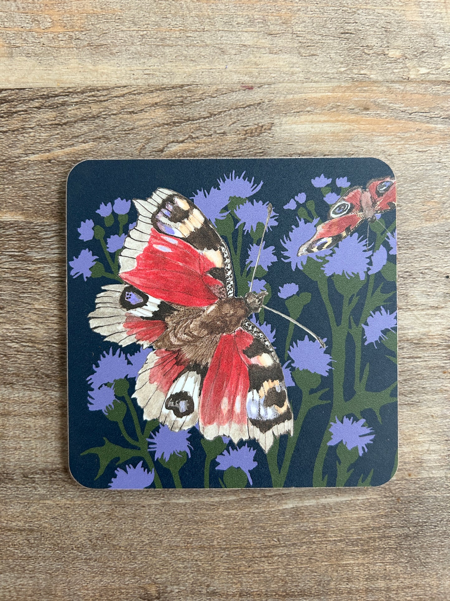 butterfly illustration on thistles, printed on coaster. Navy background with red and purple butterflies and flowers