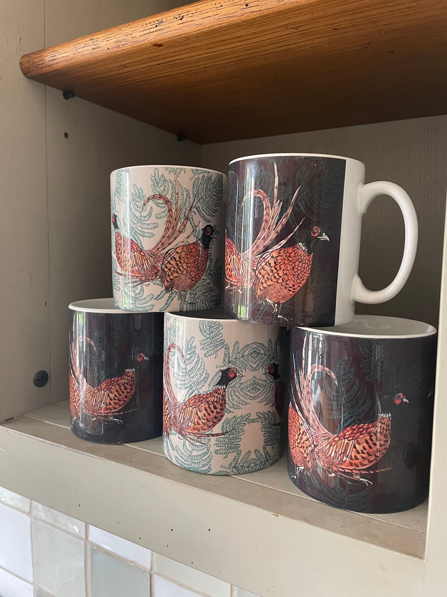 Shelf of pheasant fern illustrated mugs in brown and beige