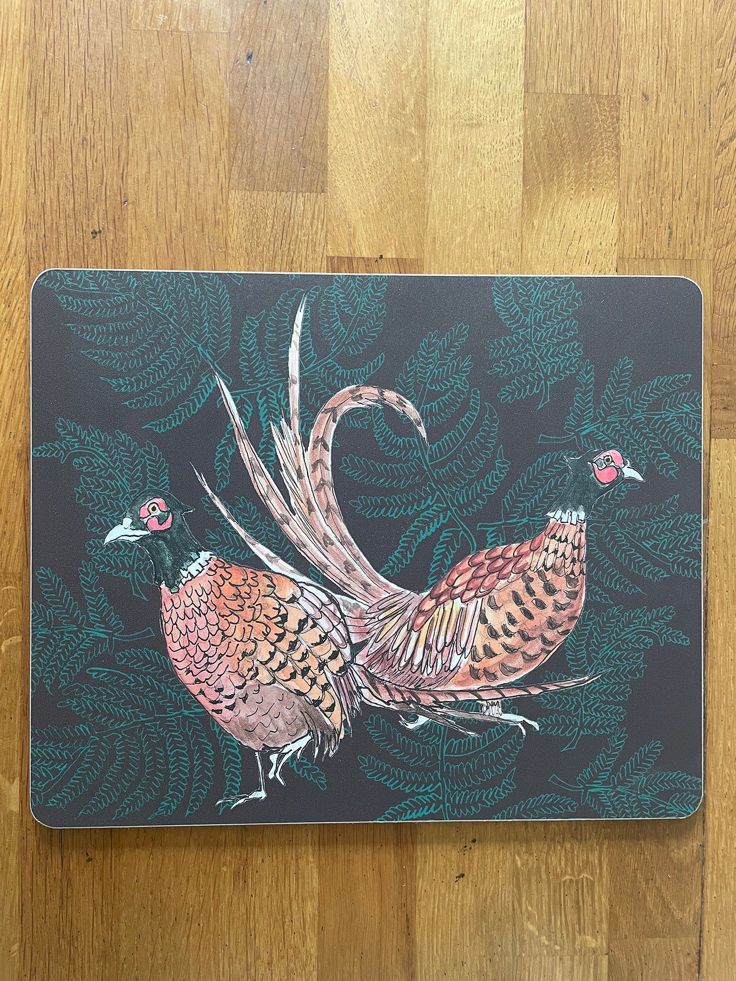 Placemat with illustration of pair of pheasants on fern background, in brown