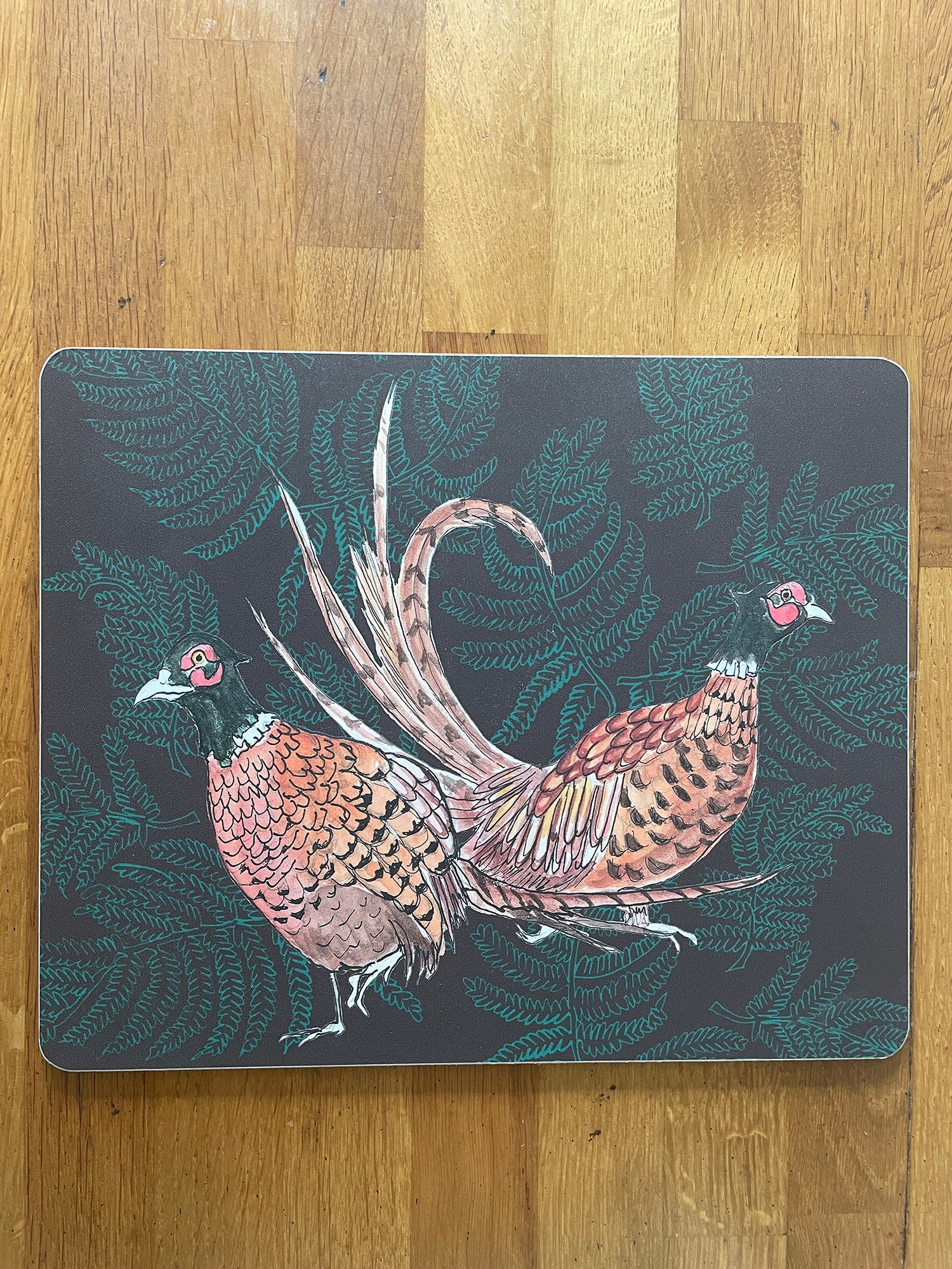 Placemat with illustration of pair of pheasants on fern background, in brown