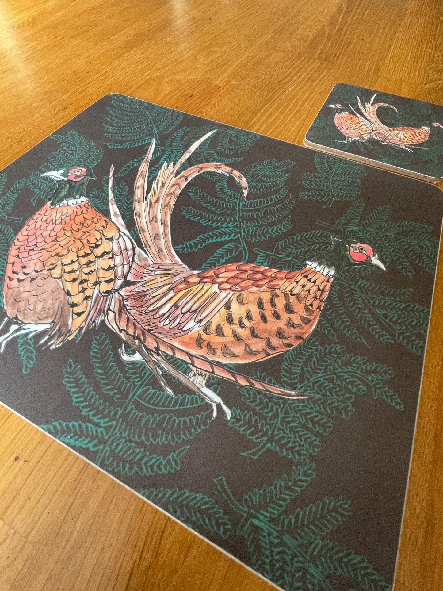 Placemat with coaster, features pheasant pair illustration on brown background with ferns