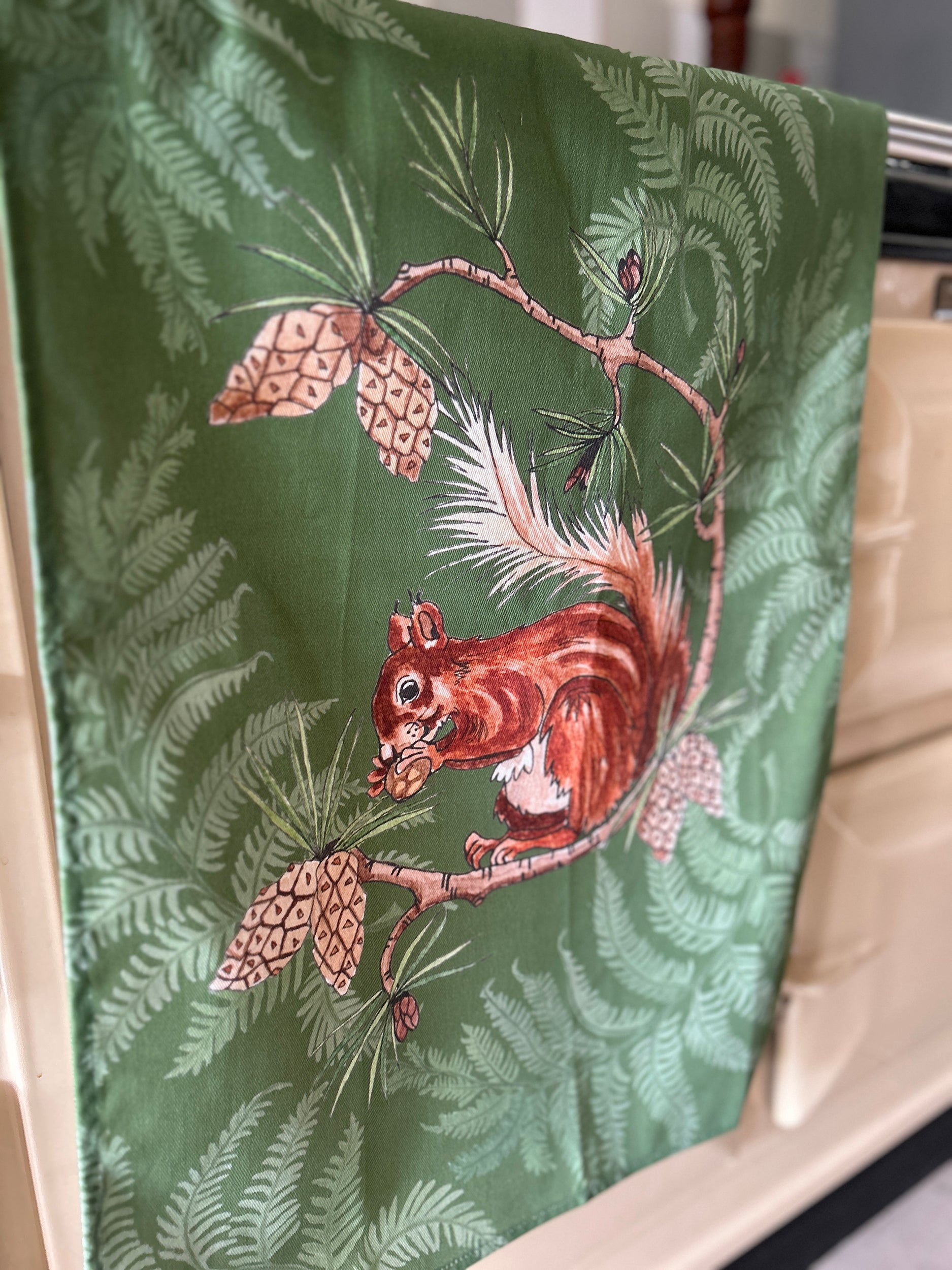 Large red squirrel illustration on green fern silhouette background tea towel