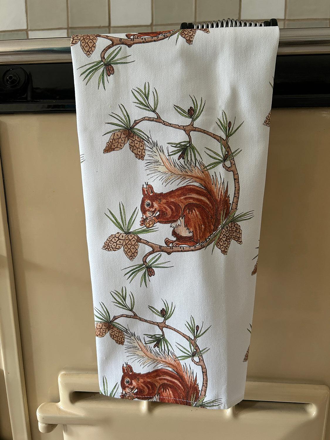 Red Squirrel illustrations printed on a white cotton tea towel hanging on an Aga stove