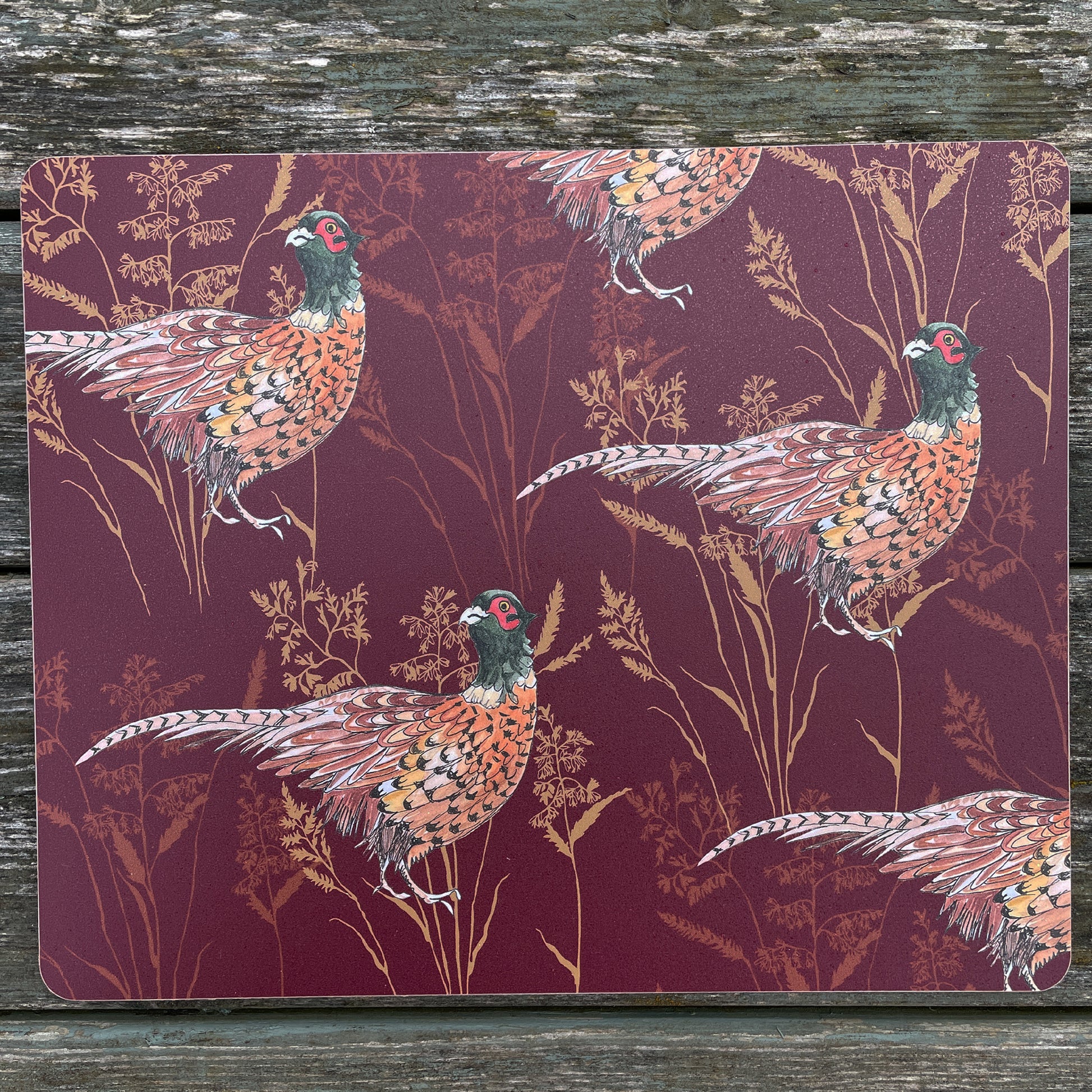 Burgundy placemat with pheasant illustration, on rustic table top