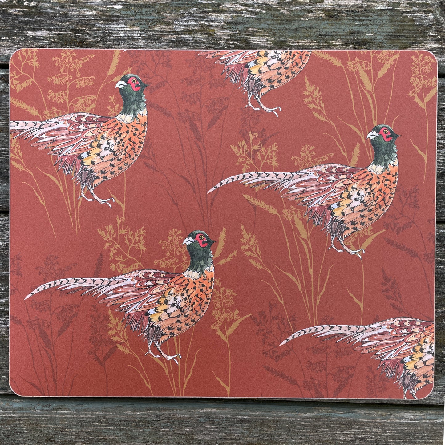 Rust coloured place mat with pheasant illustration, on rustic table top