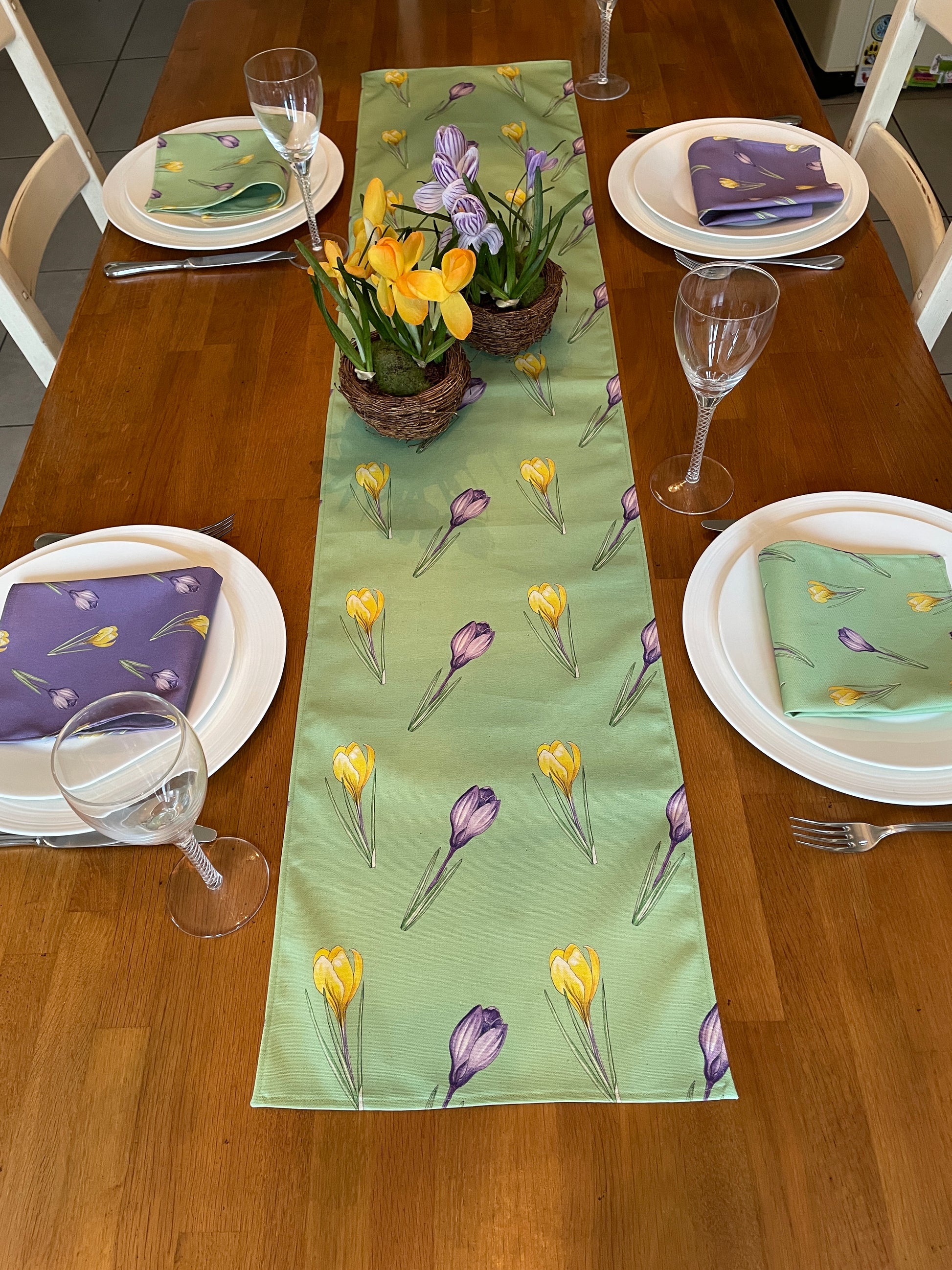 Sort crocus design, cotton table runner in green. Laid on table with four place settings with matching purple, green  napkins.